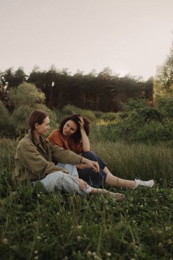 Ormanda tatilin tadını çıkaran iki mutlu beyaz kadın. Neslin neşeli güzel kızları cep telefonuyla fotoğraf çektirmek için poz veriyor. Güçlü bir kadın arkadaşlığı. Dizinin bir parçası.