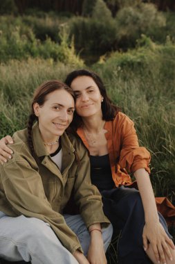 Ormanda tatilin tadını çıkaran iki mutlu beyaz kadın. Neslin neşeli güzel kızları cep telefonuyla fotoğraf çektirmek için poz veriyor. Güçlü bir kadın arkadaşlığı. Dizinin bir parçası.