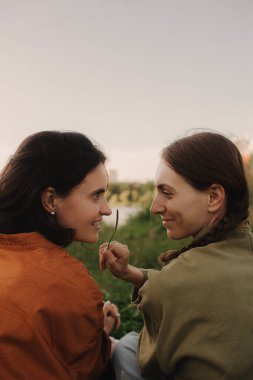 Ormanda tatilin tadını çıkaran iki mutlu beyaz kadın. Neslin neşeli güzel kızları cep telefonuyla fotoğraf çektirmek için poz veriyor. Güçlü bir kadın arkadaşlığı. Dizinin bir parçası.