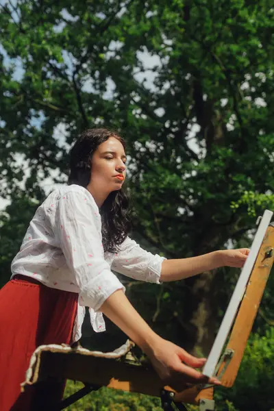 Kadın sanatçılar parkta bir resim çizerler. Farkındalık, sanat terapisi, yaratıcılık kavramı. Doğada plein hava boyama işlemi. Bir tablonun adım adım oluşturulmasını gösteren bir dizi fotoğraf.