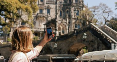 Gözlem güvertesindeki orta yaşlı gezgin kadın Portekiz 'deki Quinta da Regaleira' nın güzel bir görüntüsünü cep telefonuyla çekiyor. Seyahat ve solo turizm konsepti. Dizinin bir parçası.