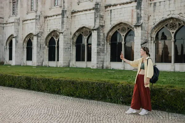 stock image Middle aged traveling woman takes pictures on a mobile phone of a beautiful view of Monteiro dos Jeronimo's in Belem, Lisbon, Portugal. Travel and solo tourism concept. Part of the series.