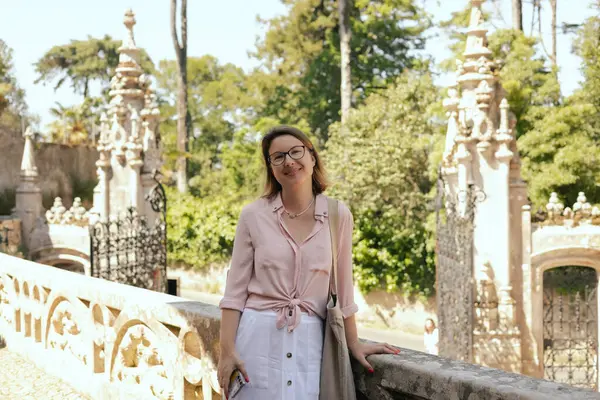 stock image Middle aged traveling woman at the observation deck takes pictures of a beautiful view of Quinta da Regaleira in Portugal on a mobile phone. Travel and solo tourism concept. Part of the series.