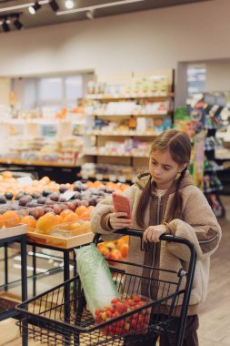 Cheerful teen girl shopping for organic fruits without plastic bags in local food store. Vegan zero waste girl choosing fresh fruits and vegetables in supermarket. Part of a series. clipart