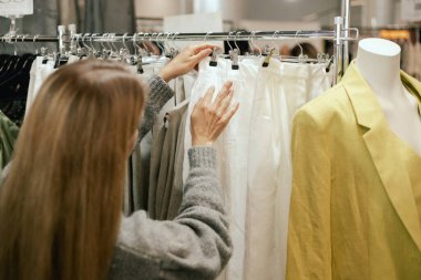 Orta yaşlı bir kadın alışveriş merkezinde bir elbise rafına doğru koşuyor. Elbise mağazasından elbise seçen kadın askısının yakın çekimi. Satış promosyonu ve alışveriş konsepti. Dizinin bir parçası.