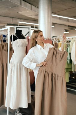 Middle aged woman chooses a dress made of natural linen in a shopping mall. Close-up of lady plucked hanger choosing clothes in clothing store. Sale promotion and shopping concept. Part of the series. clipart