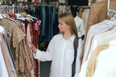 Orta yaşlı bir kadın alışveriş merkezinde doğal ketenden yapılmış bir elbise seçiyor. Elbise mağazasından elbise seçen bir hangarın yakın çekimi. Satış promosyonu ve alışveriş konsepti. Dizinin bir parçası.