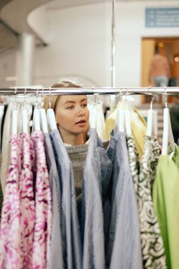 Orta yaşlı bir kadın alışveriş merkezinde doğal ketenden yapılmış bir elbise seçiyor. Elbise mağazasından elbise seçen bir hangarın yakın çekimi. Satış promosyonu ve alışveriş konsepti. Dizinin bir parçası.