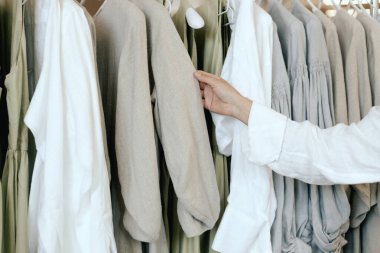 Close-up of female hands plucked hanger choosing clothes in clothing store. Middle aged woman runs across a rack of clothes in a shopping mall. Sale promotion and shopping concept. Part of the series. clipart