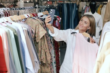 Middle aged woman takes a selfie in new clothes and sends it to her friend via phone in a shopping mall. Retail and consumerism. Sale promotion and shopping concept. Part of a series. clipart