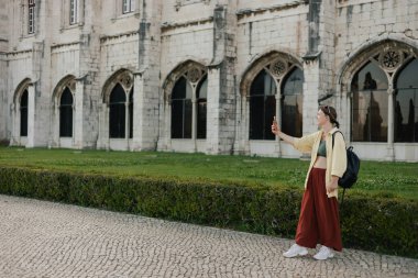 Orta yaşlı gezgin kadın, Belem, Lizbon, Portekiz 'deki Monteiro dos Jeronimo' nun güzel bir manzarasının cep telefonuyla fotoğraflarını çekiyor. Seyahat ve solo turizm konsepti. Dizinin bir parçası.