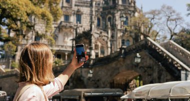 Gözlem güvertesindeki orta yaşlı gezgin kadın Portekiz 'deki Quinta da Regaleira' nın güzel bir görüntüsünü cep telefonuyla çekiyor. Seyahat ve solo turizm konsepti. Dizinin bir parçası.