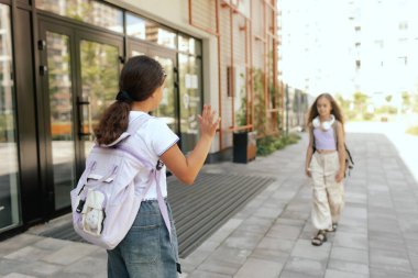 Çok ırklı ortaokul öğrencilerinin arka görünüşü, sırt çantalı sınıf arkadaşlarının açık havada birbirlerini kucaklamalarıdır. Bir serinin parçası.