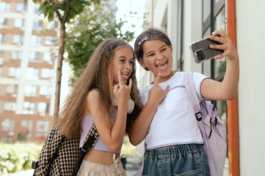 Çok ırklı ortaokul. Sırt çantalı kızlar okul bahçesinde selfie çekiyorlar. Alfa Geni. Bir serinin parçası.