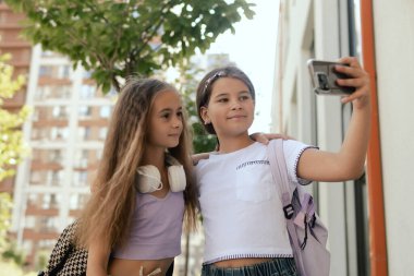 Çok ırklı ortaokul. Sırt çantalı kızlar okul bahçesinde selfie çekiyorlar. Alfa Geni. Bir serinin parçası.