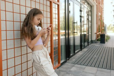 Çok ırklı ortaokul. Sırt çantalı kız arkadaşları okul bahçesindeki telefonu kullanıyor. Alfa Geni. Bir serinin parçası.