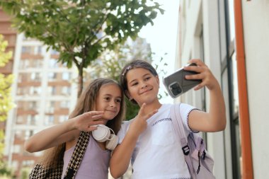 Çok ırklı ortaokul. Sırt çantalı kızlar okul bahçesinde selfie çekiyorlar. Alfa Geni. Bir serinin parçası.
