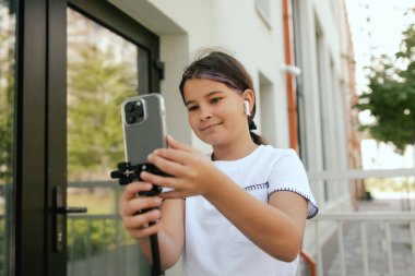 Çok ırklı ortaokul. Kız tiktok için video çekiyor ve okul bahçesinde telefon ve kulaklık kullanıyor. Alfa Geni. Dizinin bir parçası. Eğitimi ve UGC 'yi kabul et.