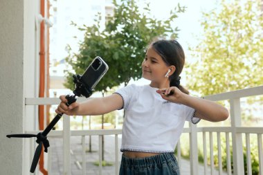 Çok ırklı ortaokul. Kız tiktok için video çekiyor ve okul bahçesinde telefon ve kulaklık kullanıyor. Alfa Geni. Dizinin bir parçası. Eğitimi ve UGC 'yi kabul et.
