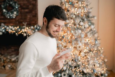 Sakallı bir adamın, Noel tebrik kartı okurken rahat oturma odasında, şenlikli bir şekilde oturduğu Noel ağacının arka planında görüntüsü. Evde mektup okumaktan hoşlanan bir bayan şaşırdım. Bir serinin parçası.