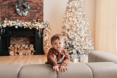 Komik çocuk oturma odasında Noel ağacının yanında oturuyor. Kış çocuklarının yaratıcılık anlayışı ve yeni yıl için hediyeler, anneler günü ve babalar günü. Modern iç mekan. Bir serinin parçası.