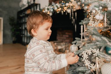 Komik çocuk oturma odasında Noel ağacının yanında oturuyor. Kış çocuklarının yaratıcılık anlayışı ve yeni yıl için hediyeler, anneler günü ve babalar günü. Modern iç mekan. Bir serinin parçası.