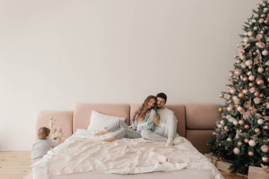 Mutlu bir aile yatakta birlikte gülüyor ve eğleniyor. İki ebeveyn evde oğluyla oynuyor. Anne ve baba hafta sonları çocuklarıyla kaliteli zaman geçiriyorlar. Bir serinin parçası.