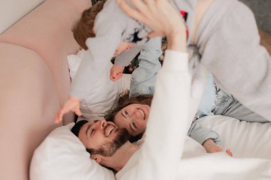 Mutlu bir aile yatakta birlikte gülüyor ve eğleniyor. İki ebeveyn evde oğluyla oynuyor. Anne ve baba hafta sonları çocuklarıyla kaliteli zaman geçiriyorlar. Bir serinin parçası.