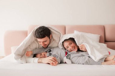 Mutlu bir aile yatakta birlikte gülüyor ve eğleniyor. İki ebeveyn evde oğluyla oynuyor. Anne ve baba hafta sonları çocuklarıyla kaliteli zaman geçiriyorlar. Bir serinin parçası.