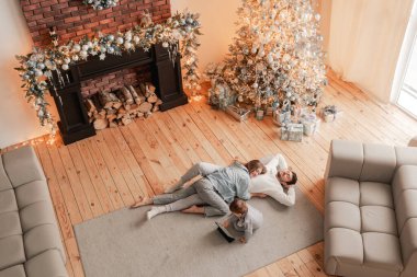 Mutlu bir aile birlikte gülüyor ve eğleniyor. İki ebeveyn ve oğulları oturma odasında yerde yatıyorlar. Annem ve babam hafta sonları çocuklarla iyi vakit geçiriyorlar. Yukarıdan görüntüle.