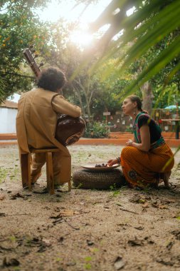 Indian musician in traditional clothes playing sitar festive season outdoor home. Woman in traditional saree hand lighting Diya lamp during Diwali festival. Happy greeting photo. Part of a series. clipart