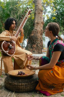 Indian musician in traditional clothes playing sitar festive season outdoor home. Woman in traditional saree hand lighting Diya lamp during Diwali festival. Happy greeting photo. Part of a series. clipart