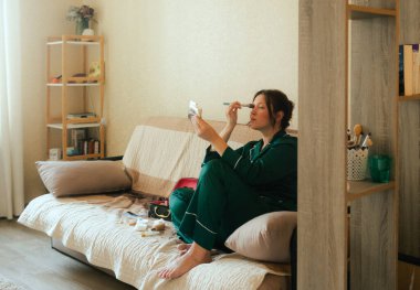 Artı, sosyal medya için akıllı telefondan vlog kaydederken yüzüne fırçayla makyaj yapan boyda bir kadın. Çok ırklı makyaj sanatçısı vlogger canlı yayın makyaj eğitmeni. Dizinin bir parçası. UGC.