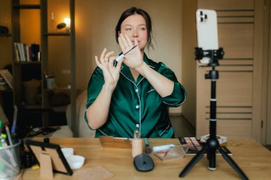 Artı, sosyal medya için akıllı telefondan vlog kaydederken yüzüne fırçayla makyaj yapan boyda bir kadın. Çok ırklı makyaj sanatçısı vlogger canlı yayın makyaj eğitmeni. Dizinin bir parçası. UGC.