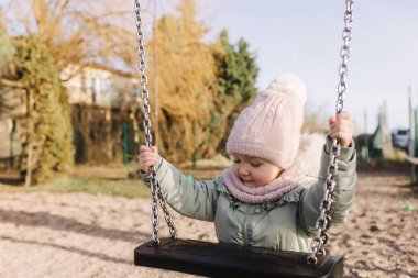 Mutlu gülümseyen tatlı kız, kreş kızı oynayan çocuk, çocuk parkında salıncakta sallanıyor, çocuk gelişimi için konsept görüntü, güneş ışığı altında dışarıda oynayan sağlıklı çocuk.