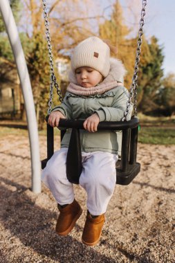 Mutlu gülümseyen tatlı kız, kreş kızı oynayan çocuk, çocuk parkında salıncakta sallanıyor, çocuk gelişimi için konsept görüntü, güneş ışığı altında dışarıda oynayan sağlıklı çocuk.