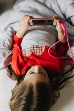 Güzel genç kız telefonda uygulama kullanıyor, çevrimiçi video görüşmesi yapıyor, gülüyor, gizlice film izliyor, çevrimiçi oyunlar oynuyor, örtünün altında yatıyor. Jenerasyon alfa kavramı. Bir serinin parçası