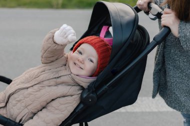 Sıcak paltolu genç annenin bebek arabasını iterken ve yaya geçidinde yavaşça caddeyi geçerken. Şehir hayatı. Yan görüş. Tek başına ebeveynlik ve çocuk yetiştirme kavramı. Bir serinin parçası