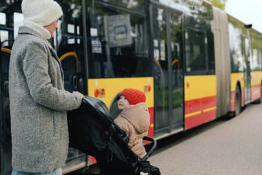 Bebek arabalı anne istasyonda otobüse biniyor. Şehirde pusetli bir kadın var. Alt kat otobüsü. Yakın plan. Tek başına ebeveynlik ve şehir ulaşımı kavramı. Bir serinin parçası