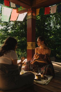 Düşünceli meditasyon ve çardakta yoga yapmadan önce kadın akıl hocası ve öğrenciyi kapatın. Meditasyon deneyimini kolaylaştırmak. Dizinin bir parçası. Tibet şarkı kasesi. Yumuşak odak, bulanık, gürültü efekti