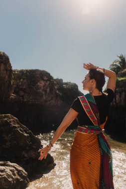 Geleneksel sari elbiseli Hintli kadın, arka planda okyanus varken doğada geleneksel danslar yapıyor. Hint festivali kostümü. Yalnız turizm kavramı ve Hindistan 'a seyahat. Bir serinin parçası