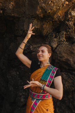 Geleneksel sari elbiseli Hintli kadın, arka planda okyanus varken doğada geleneksel danslar yapıyor. Hint festivali kostümü. Yalnız turizm kavramı ve Hindistan 'a seyahat. Bir serinin parçası