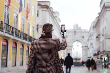 Vlogger gezgini kadın Lizbon 'a seyahat tatilini uygulayarak telefon paylaşımına video kaydediyor. Ticaret Meydanı 'na giden yolda sosyal medya hikayeleri çeken orta yaşlı bir kadın. UGC