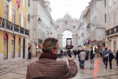 Vlogger gezgini kadın Lizbon 'a seyahat tatilini uygulayarak telefon paylaşımına video kaydediyor. Ticaret Meydanı 'na giden yolda sosyal medya hikayeleri çeken orta yaşlı bir kadın. UGC