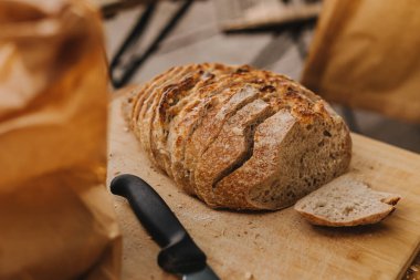 Ahşap bir masada bıçakla tam tahıllı ekmeği kesen şefin ellerine yakın çekim. Sağlıklı beslenme ve geleneksel fırın kavramı. Seçici odak