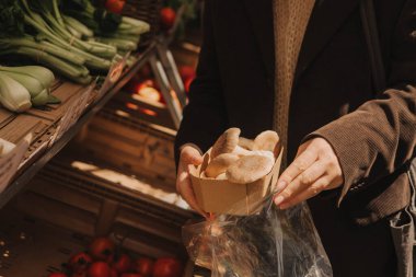 Yerel çiftçi pazarında, polietilen çantasındaki egzotik mantarlarla el ele tutuşun. Olgun Kadın Müşteri Dükkanı 'ndan alışveriş yapıyor. Sebze alan kadın. Kapatın. Dizinin bir parçası