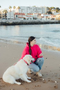 Genç bir kadın, güneşli bir havada okyanus sahilinde Golden Retriever köpeği eğitiyor. Mutlu köpekler konsepti. Bir serinin parçası