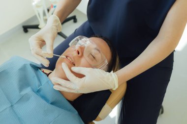 Genç bir dişçiye dişçi muayenesinde gülümseyen olgun bir kadın. Klinikte randevu. Diş beyazlatma, temizlik ya da oral, hastanede ağız ve sakız bakımı. Yumuşak odaklanma. Dizinin bir parçası. Yakın plan..