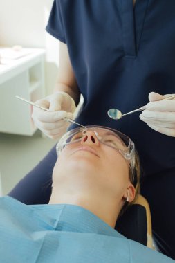 Genç bir dişçiye dişçi muayenesinde gülümseyen olgun bir kadın. Klinikte randevu. Diş beyazlatma, temizlik ya da oral, hastanede ağız ve sakız bakımı. Yumuşak odaklanma. Dizinin bir parçası. Yakın plan..