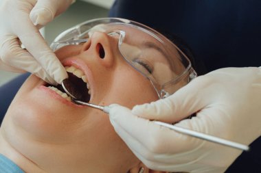 Genç bir dişçiye dişçi muayenesinde gülümseyen olgun bir kadın. Klinikte randevu. Diş beyazlatma, temizlik ya da oral, hastanede ağız ve sakız bakımı. Yumuşak odaklanma. Dizinin bir parçası. Yakın plan..